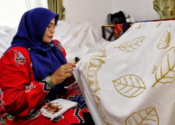 Seorang pengrajin Batik Mandau dari Kabupaten Bengkalis sedang tekun membuat pola pada kain putih. Ia mengaplikasikan lilin panas menggunakan alat canting untuk membentuk motif pada kain, motif yang sedang dibuat mencakup unsur daun, pompa migas, hingga ornamen-ornamen melayu yang akan menjadi kain Batik Mandau binaan PHR Zona Rokan